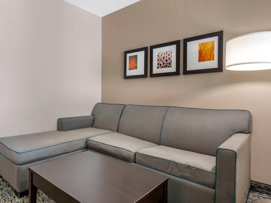 Habitación de hotel con un sofá seccional gris, una pequeña mesa de centro de madera y tres obras de arte enmarcadas en la pared.