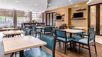 Un interior de restaurante moderno con varias mesas y sillas, ventanas amplias y un televisor de pantalla plana en la pared.