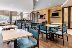 L’intérieur d’un restaurant moderne, avec de nombreuses tables et chaises, de grandes fenêtres et un téléviseur à écran plat fixé au mur.