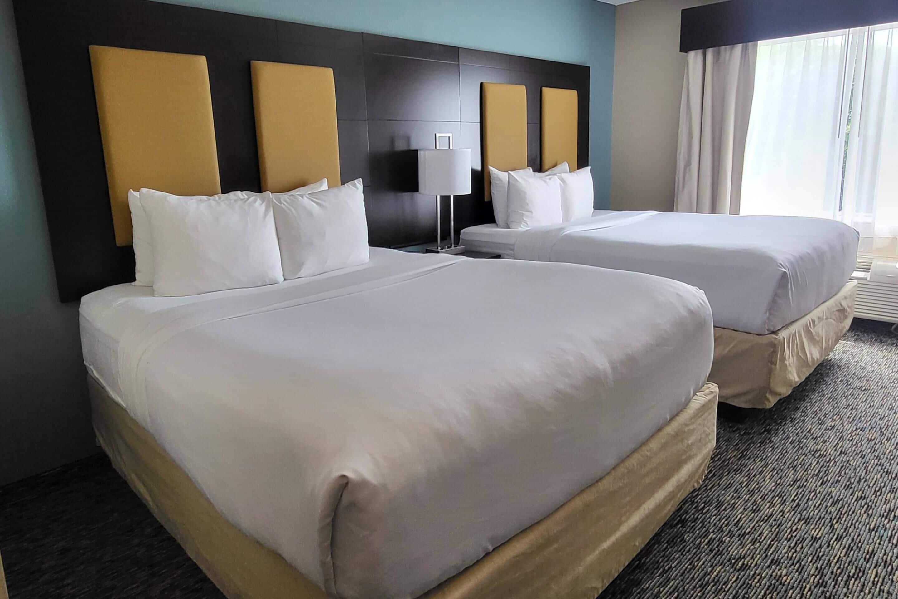 Una habitación de hotel con dos camas, una mesita de noche, una lámpara y una ventana con cortinas.