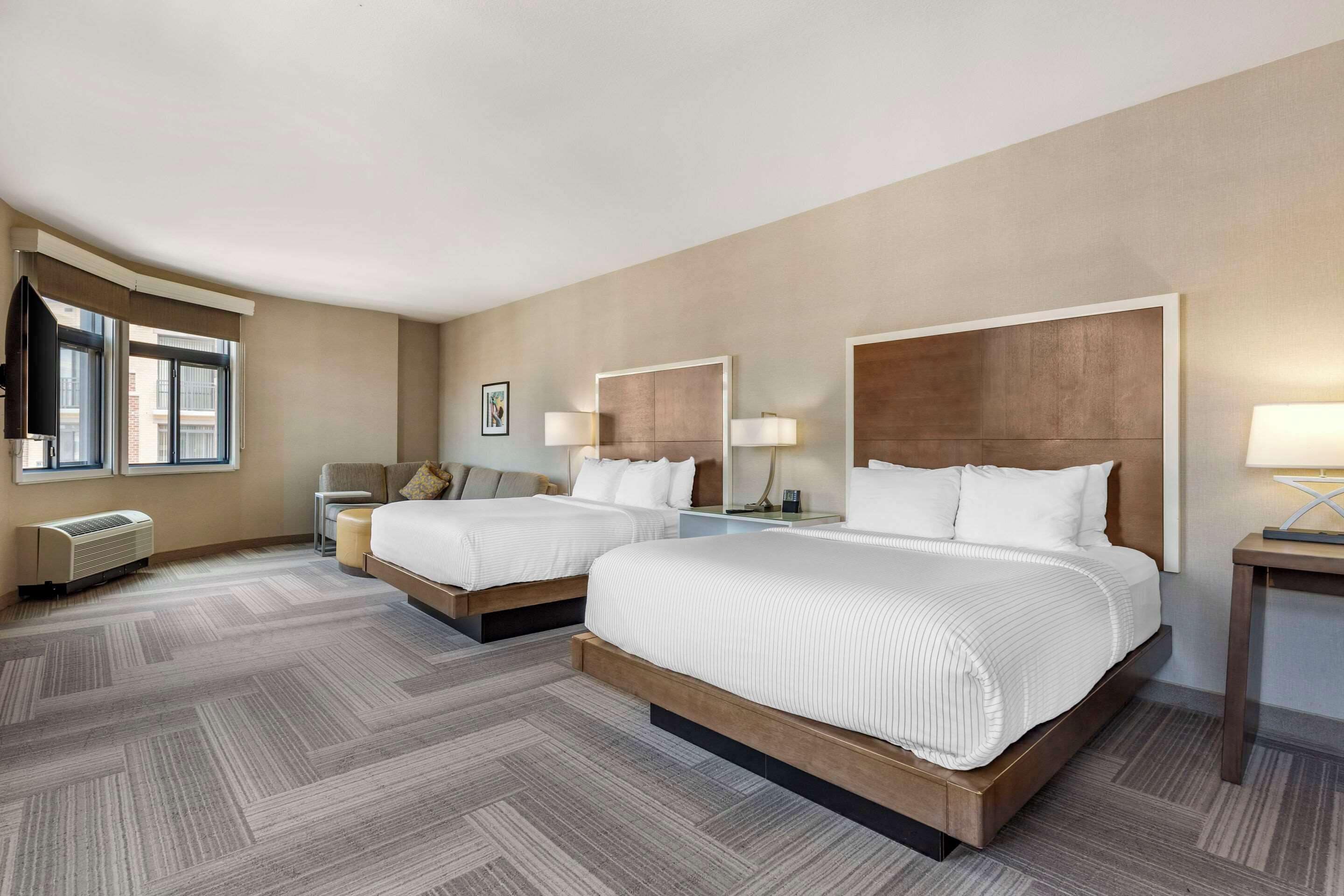 Habitación de hotel con dos camas, un escritorio, una silla y una ventana con cortinas.