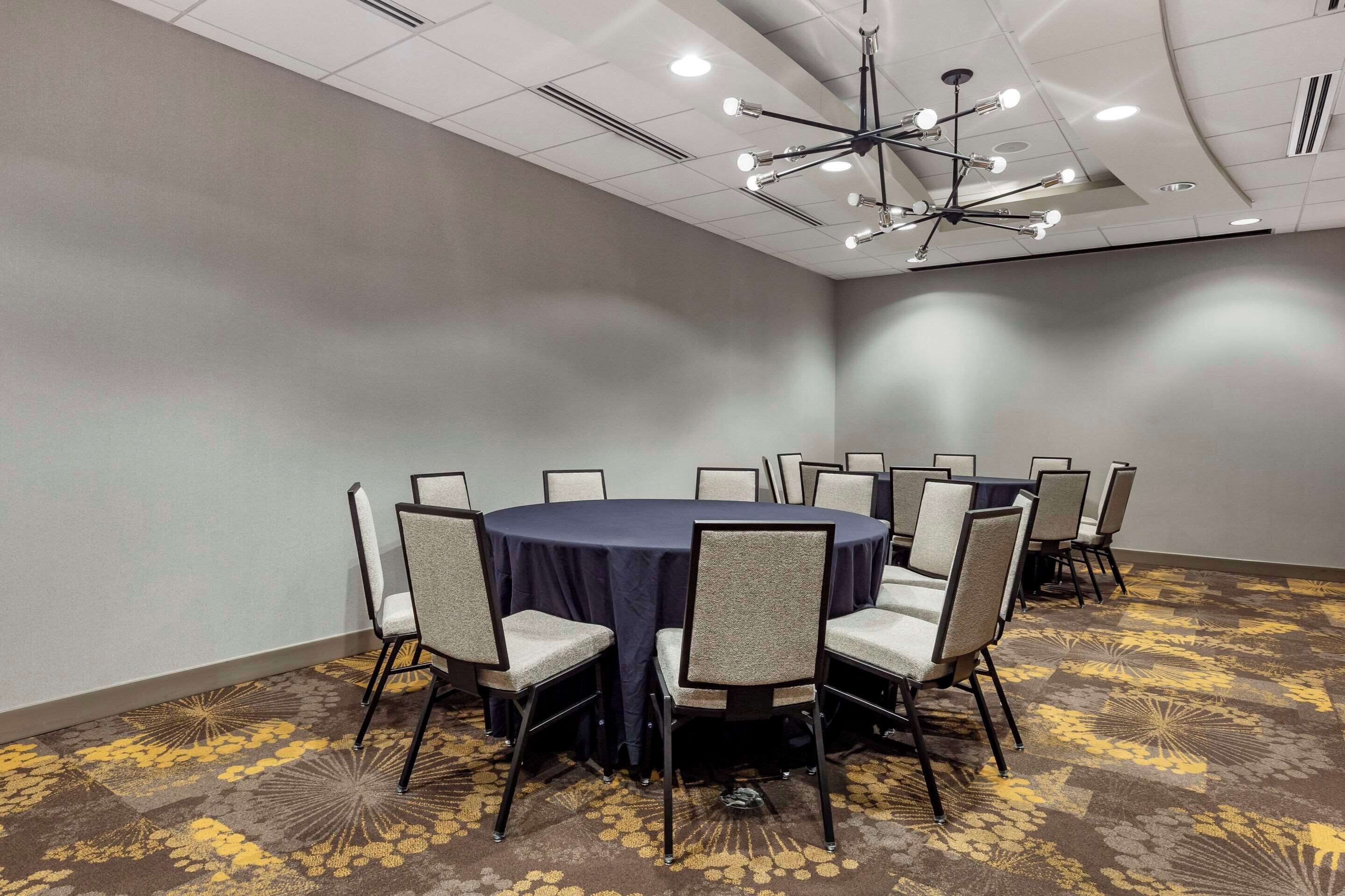A conference room with a round table, chairs, a ceiling light fixture, and patterned carpet.