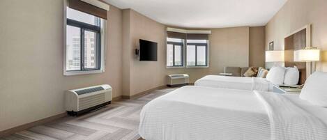 A hotel room with two beds, a flat-screen TV, a window, a heater, and a lamp.