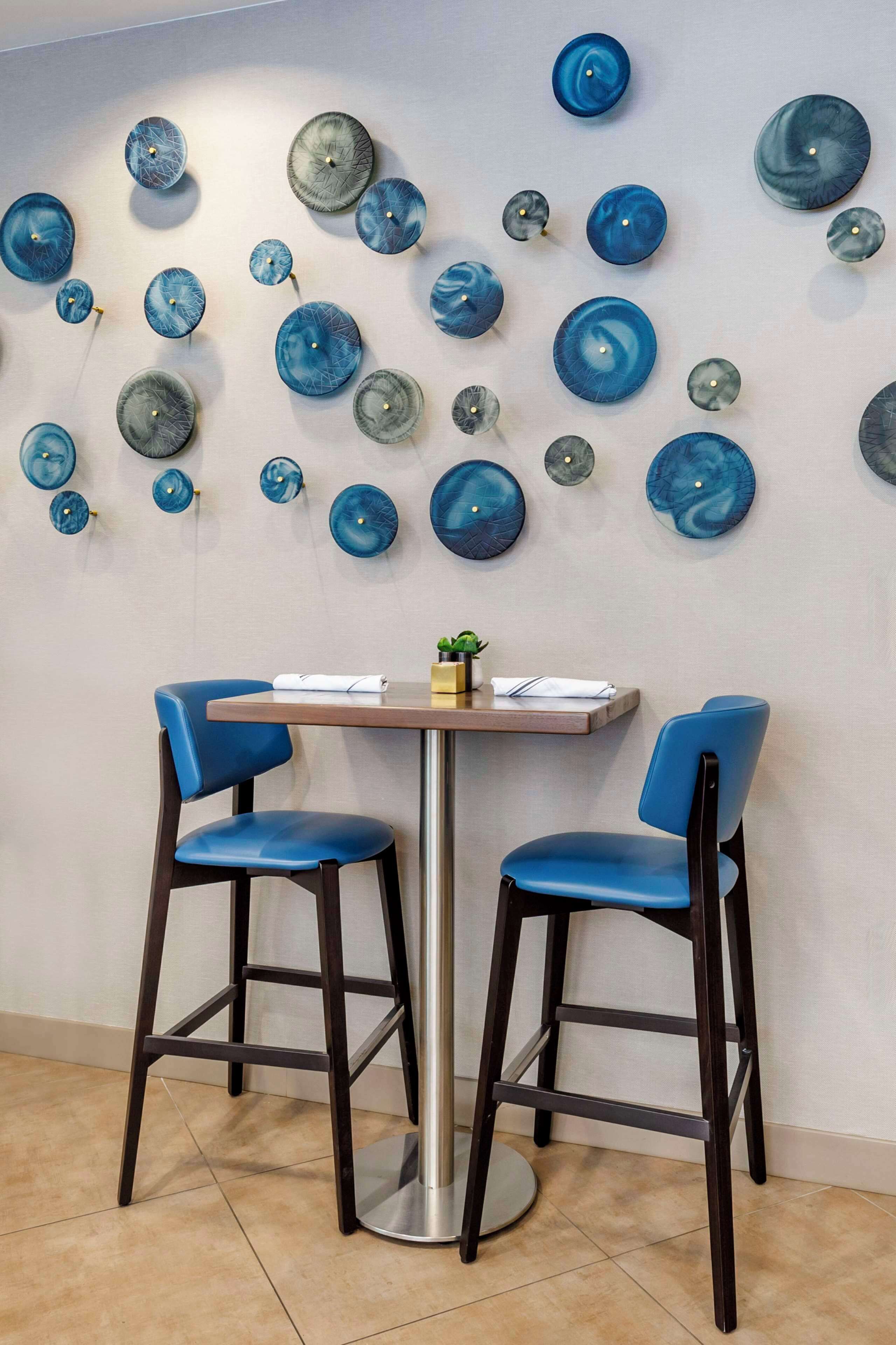 Un comedor con dos sillas azules, una mesita y una pared decorada con platos azules y grises.