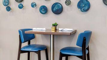 Un comedor con dos sillas azules, una mesita y una pared decorada con platos azules y grises.