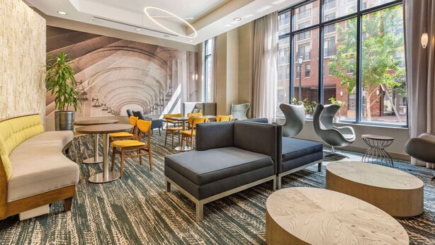 A modern hotel lobby with a curved wall mural, seating areas, and large windows offering a view of the city.