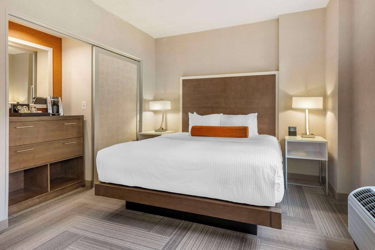 Een moderne hotelkamer met een groot bed, een houten garderobe, nachtkastjes met lampen en een ingebouwde airconditioning.