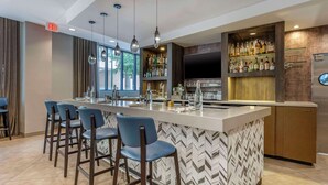 A modern bar area with a long counter, bar stools, and a variety of bottles and glasses.