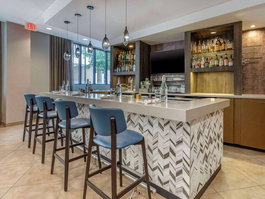 A modern bar area with a long counter, bar stools, and a variety of bottles and glasses.