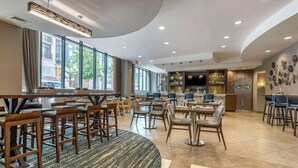 A modern hotel lobby with a bar area, seating arrangements, and large windows offering views of the street.