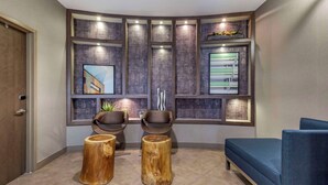 A modern waiting area with a curved wall, two wooden stools, a blue sofa, and framed artwork.