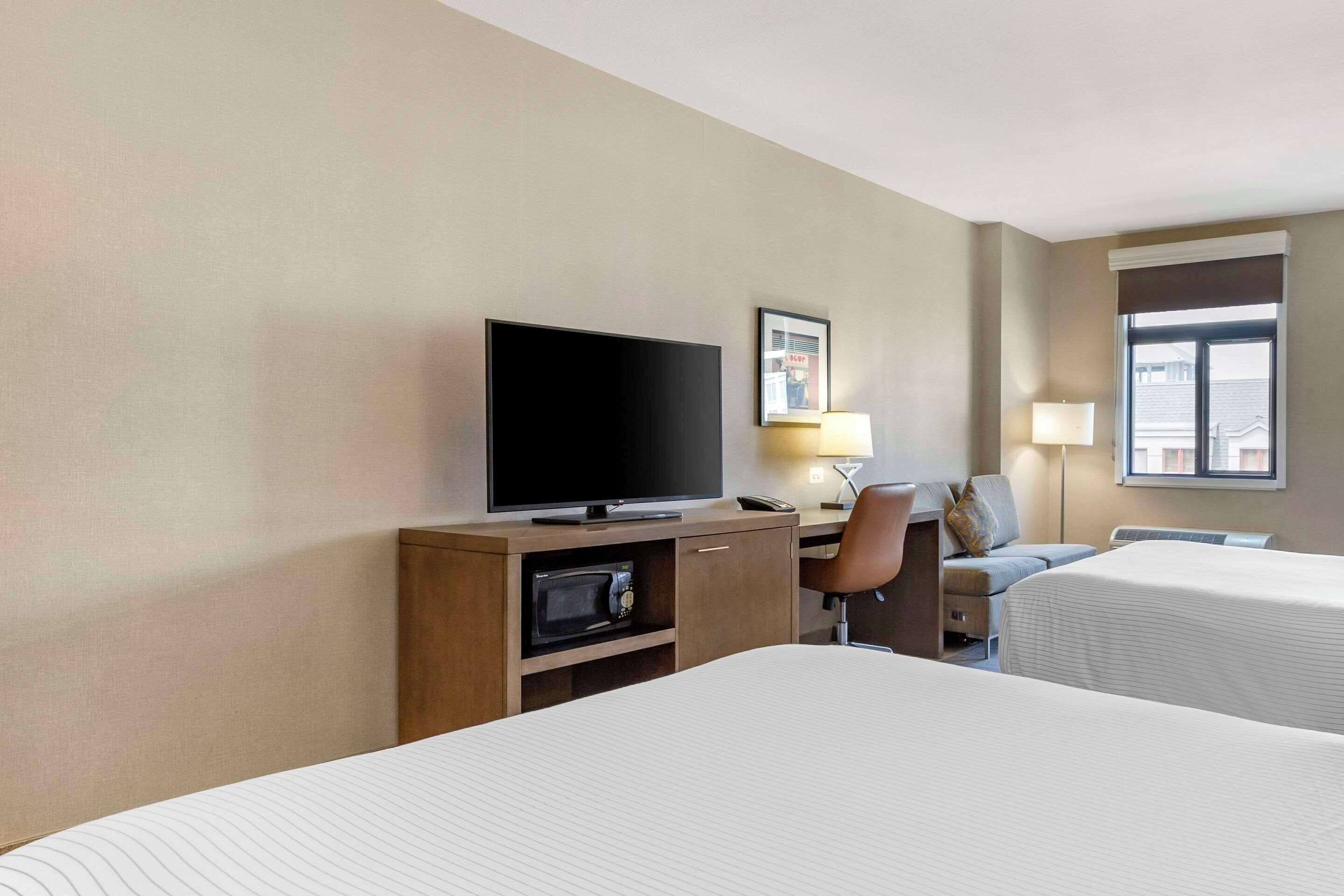 Habitación de hotel con dos camas, un televisor, un escritorio con lámpara y una ventana.