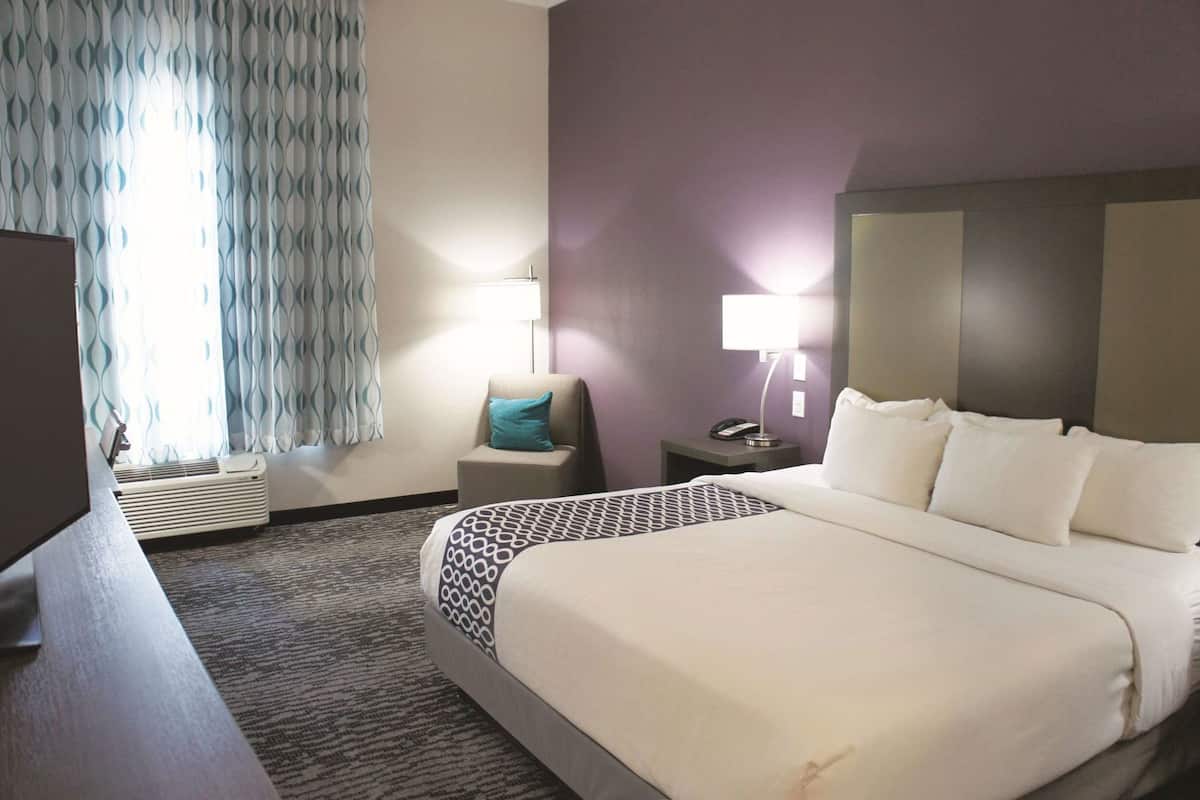 Une chambre d’hôtel avec un grand lit, une chaise, un bureau, une lampe et un téléphone sur une table de chevet.