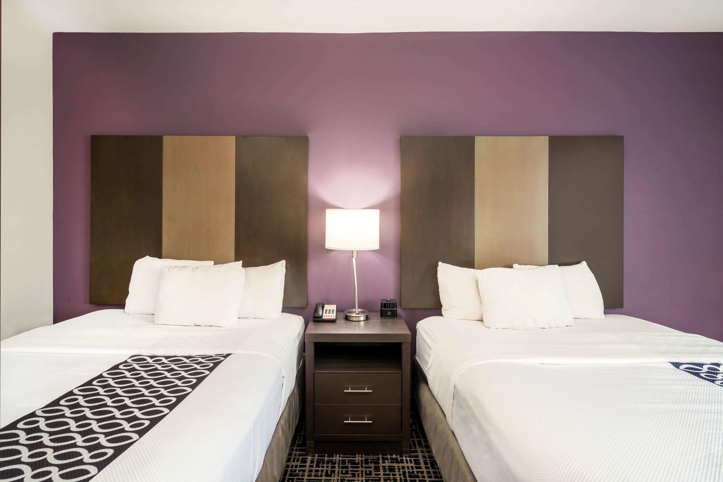 A hotel room with two beds, a nightstand with a lamp, and a patterned runner.