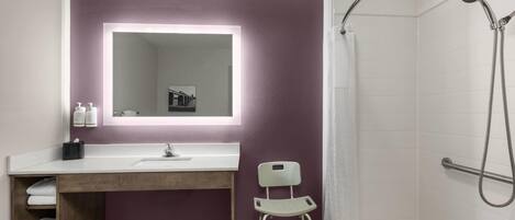 Une salle de bain équipée d’un meuble-lavabo, d’une douche et d’un siège accessible aux personnes en fauteuil roulant.