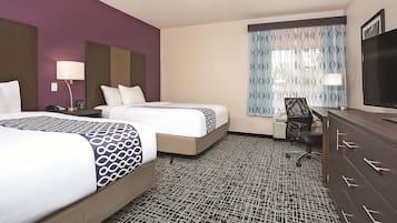 A hotel room with two beds, a desk, a chair, a TV, and a patterned carpet.