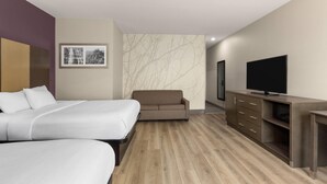 Une chambre d’hôtel avec deux lits, un canapé, une télévision et un plancher en bois.