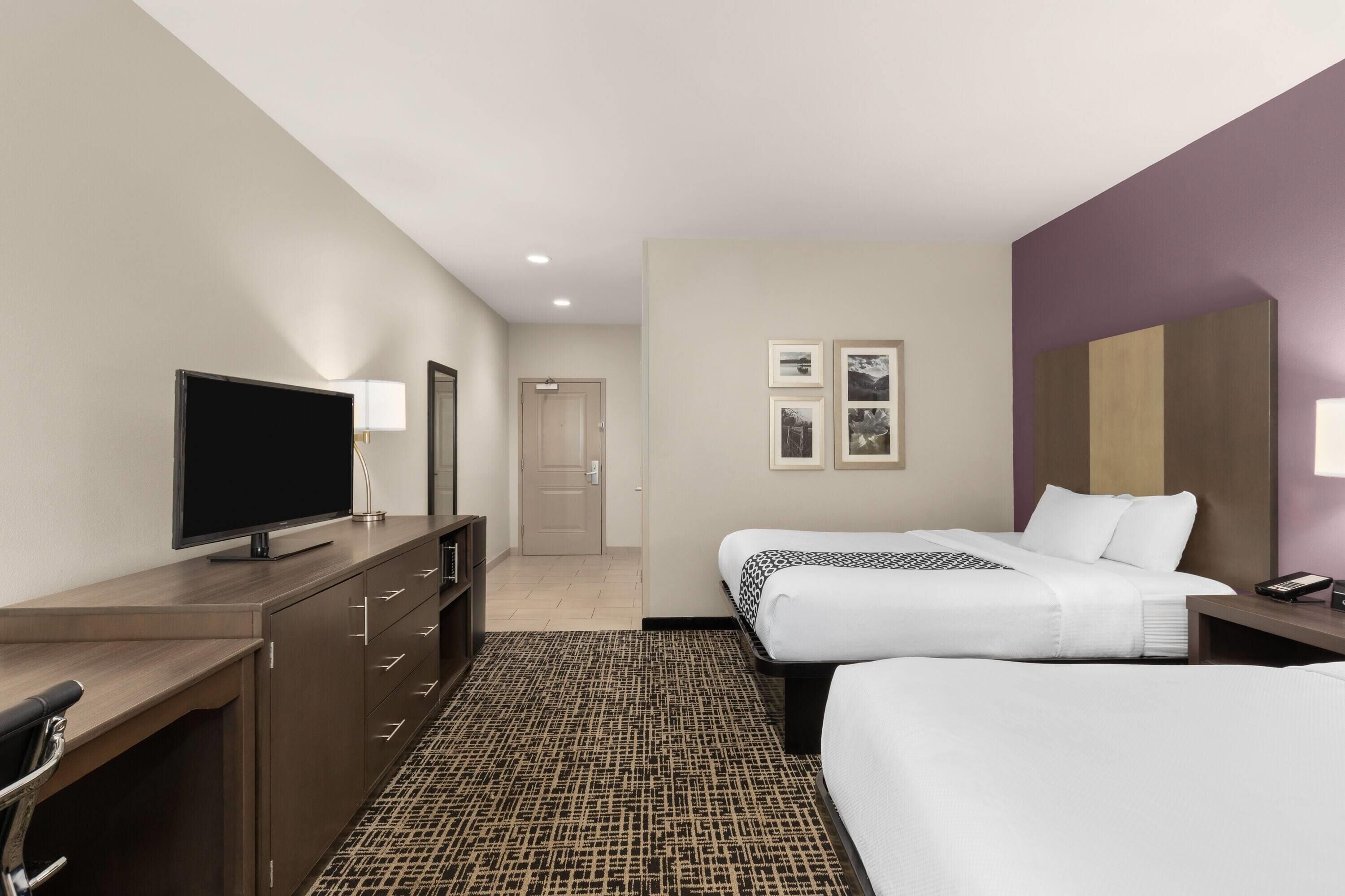 Habitación de hotel con dos camas, un escritorio, un televisor de pantalla plana, un aparador y una alfombra estampada.