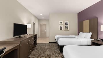 Habitación de hotel con dos camas, un escritorio, un televisor de pantalla plana, un aparador y una alfombra estampada.