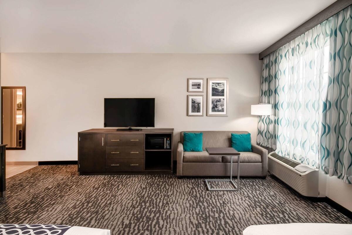Une chambre d’hôtel équipée d’un téléviseur à écran plat, d’un canapé avec des coussins de couleur turquoise, d’une petite table et d’un tapis à motifs.