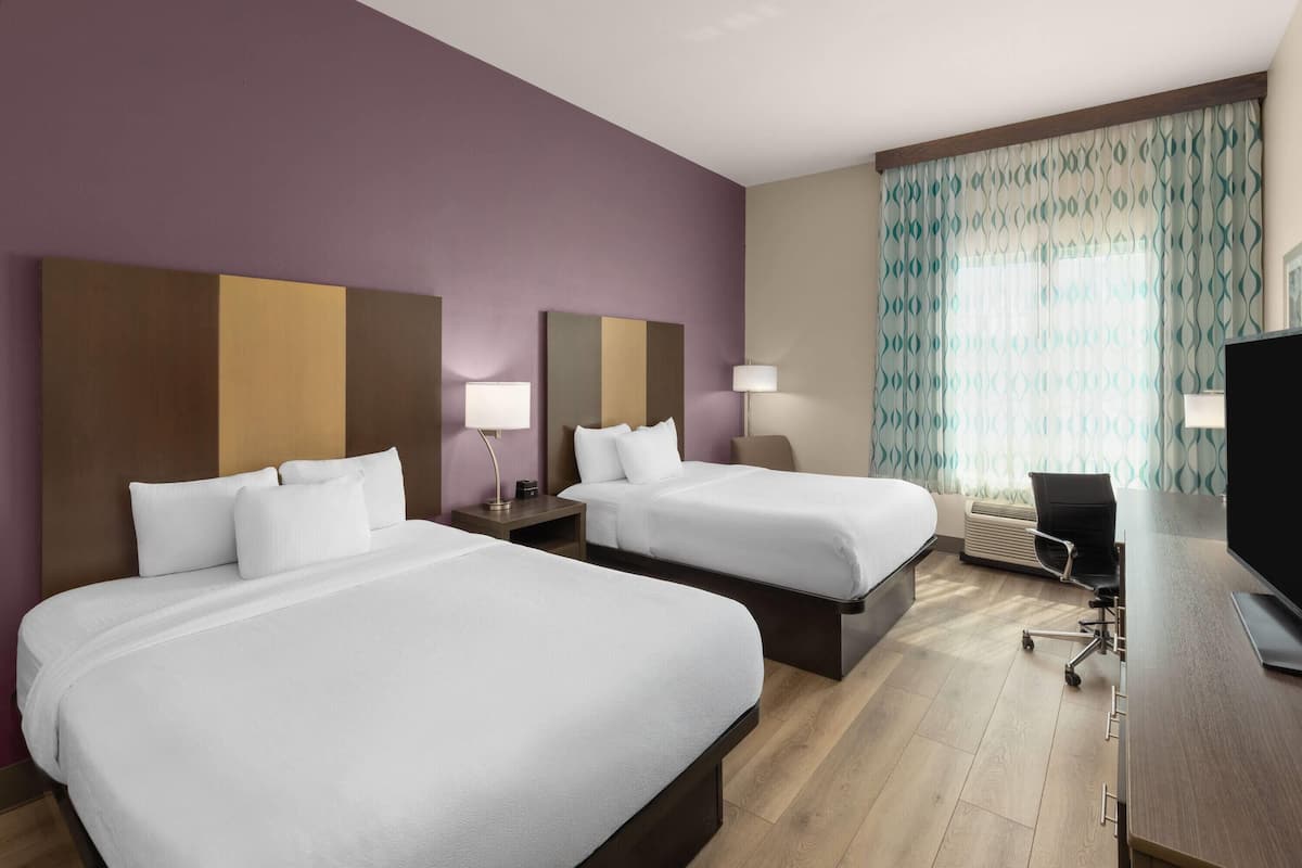 Une chambre d’hôtel avec deux lits, un bureau, une chaise et un téléviseur.