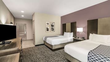 A hotel room with two beds, a TV, a desk, and a patterned carpet.
