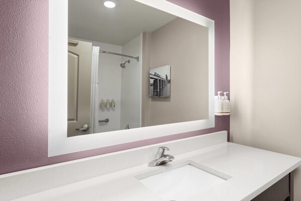 Un baño con un lavamanos blanco, un espejo grande y una zona de ducha visible en el reflejo.