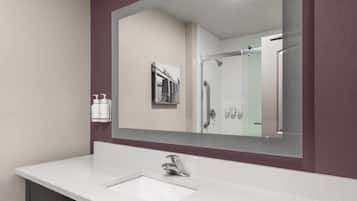 Un baño con un lavamanos blanco, un espejo grande y una cabina de ducha con paredes de vidrio.