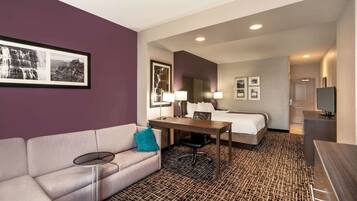 Une chambre d’hôtel avec un canapé, une petite table, un lit, un bureau et une télévision.