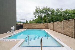Una piscina rectangular con pared de piedra y barandillas metálicas.