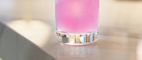 A tall glass with a pink drink, ice cubes, and a lime garnish on a bar counter.