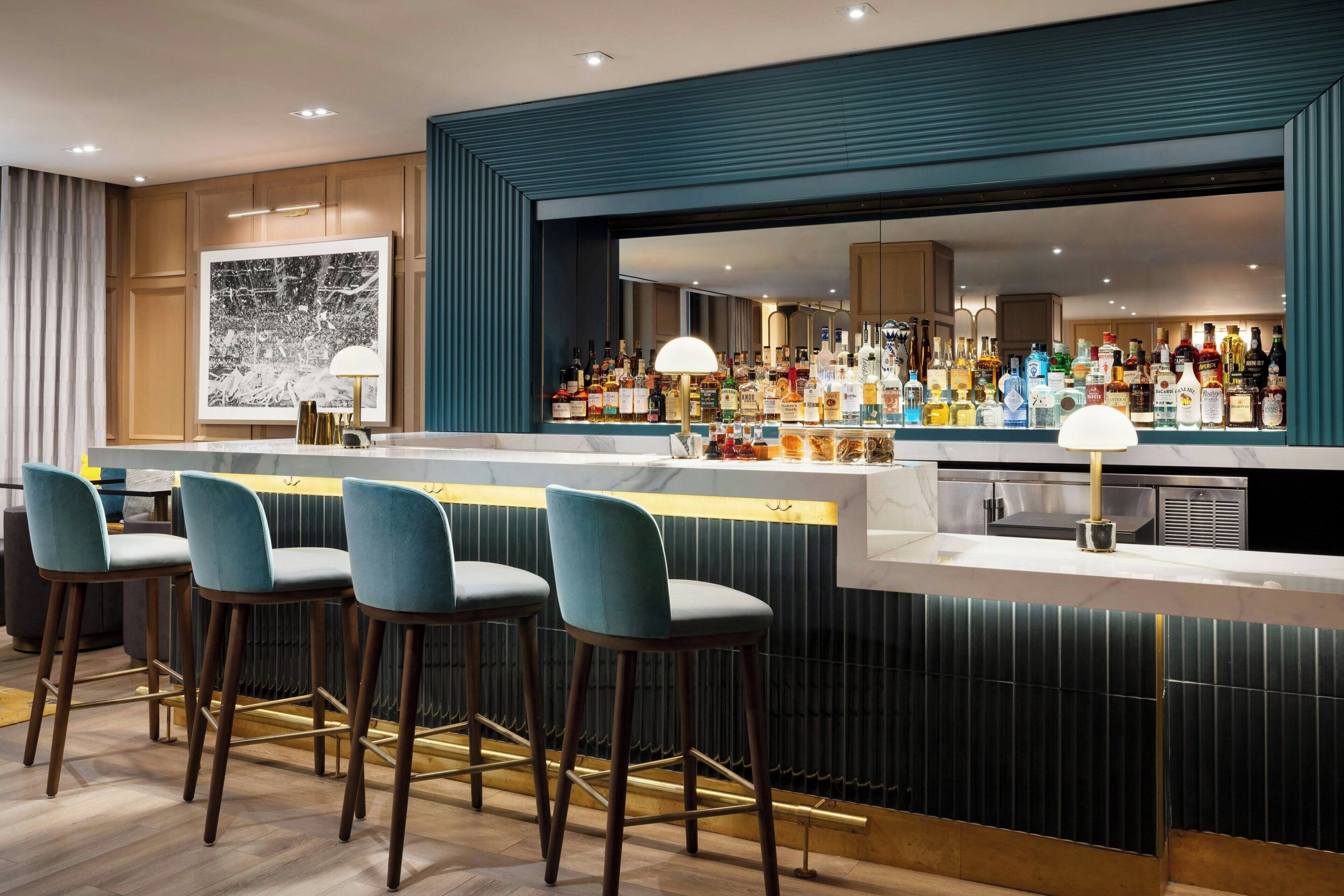 A bar area with a long counter, multiple stools, and a variety of bottles.