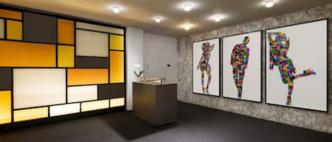 Un área de recepción moderna con un diseño geométrico en la pared, un mostrador de recepción y tres piezas de arte abstracto de colores en la pared.