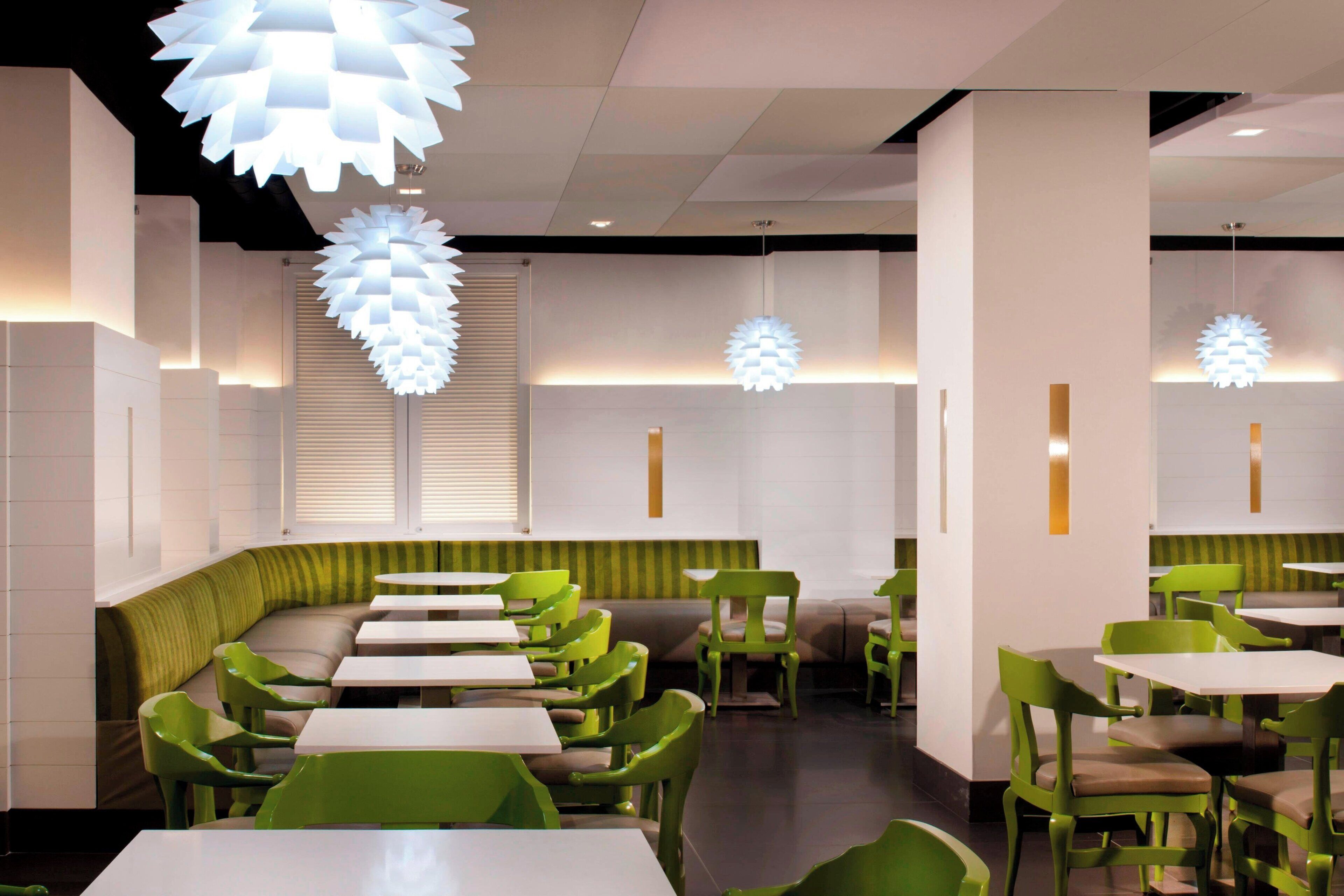 A modern restaurant interior with green seating and white tables, featuring unique spherical pendant lights.