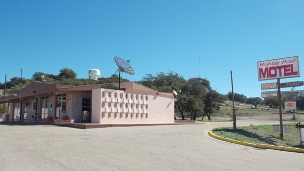 A Holiday Host Motel with a satellite dish, a water tank, and a signboard advertising amenities like phones, TV, and a swimming pool. - Holiday Host Motel (Sonora)