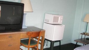 A compact room with a wooden desk, a television, a microwave, and a chair. - Holiday Host Motel (Sonora)