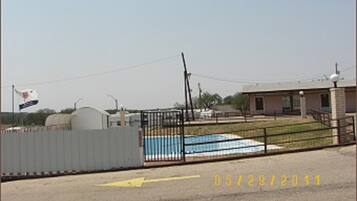 A fenced outdoor area with a swimming pool, a building, and a flag.