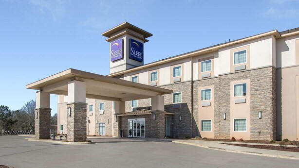A Sleep Inn & Suites building with a covered entrance, stone facade, and multiple windows. - Sleep Inn & Suites Meridian - Bonita Lakes (Meridian)