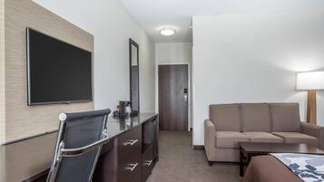 A hotel room with a bed, a sofa, a desk with a chair, a flat-screen TV, and a mirror.