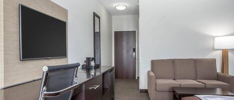 A hotel room with a bed, a sofa, a desk with a chair, a flat-screen TV, and a mirror.