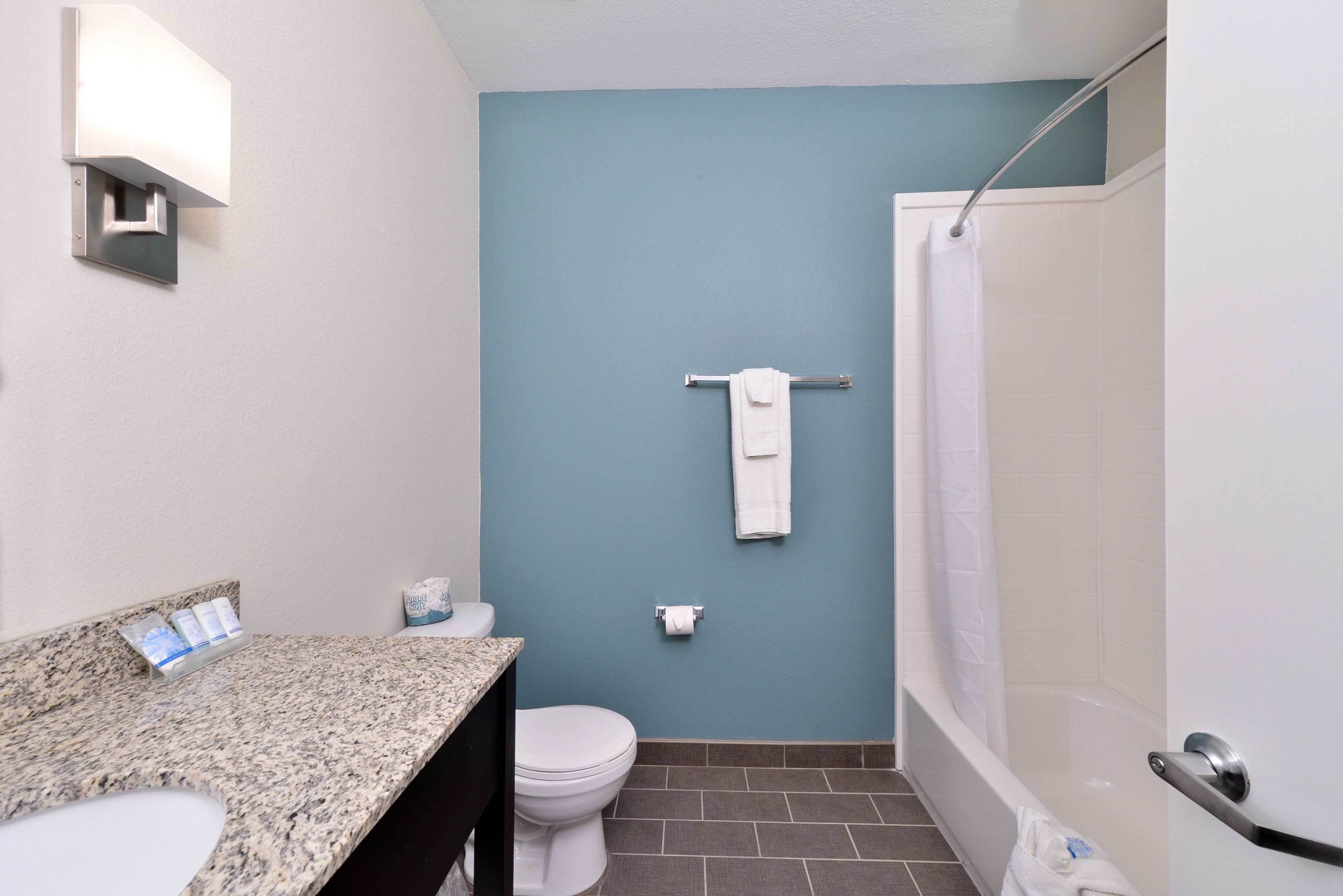 Un baño con pared azul, inodoro blanco, lavabo con encimera de granito y zona de ducha.