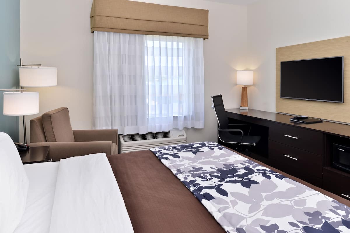 A hotel room with a bed, a desk, a chair, a TV, and a window with curtains.