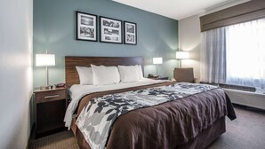 A hotel room with a large bed, two bedside lamps, a nightstand, a chair, and a window with curtains. - Sleep Inn & Suites Meridian - Bonita Lakes (Meridian)