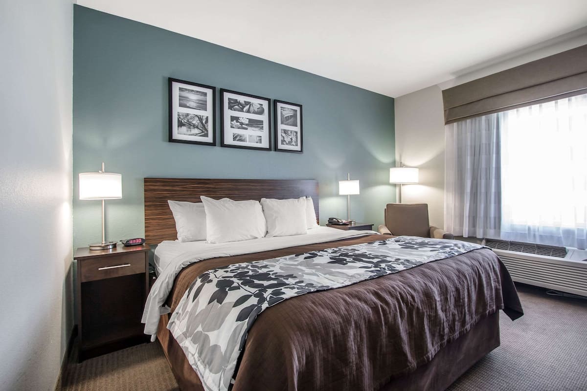 A hotel room with a large bed, two bedside lamps, a nightstand, a chair, and a window with curtains.