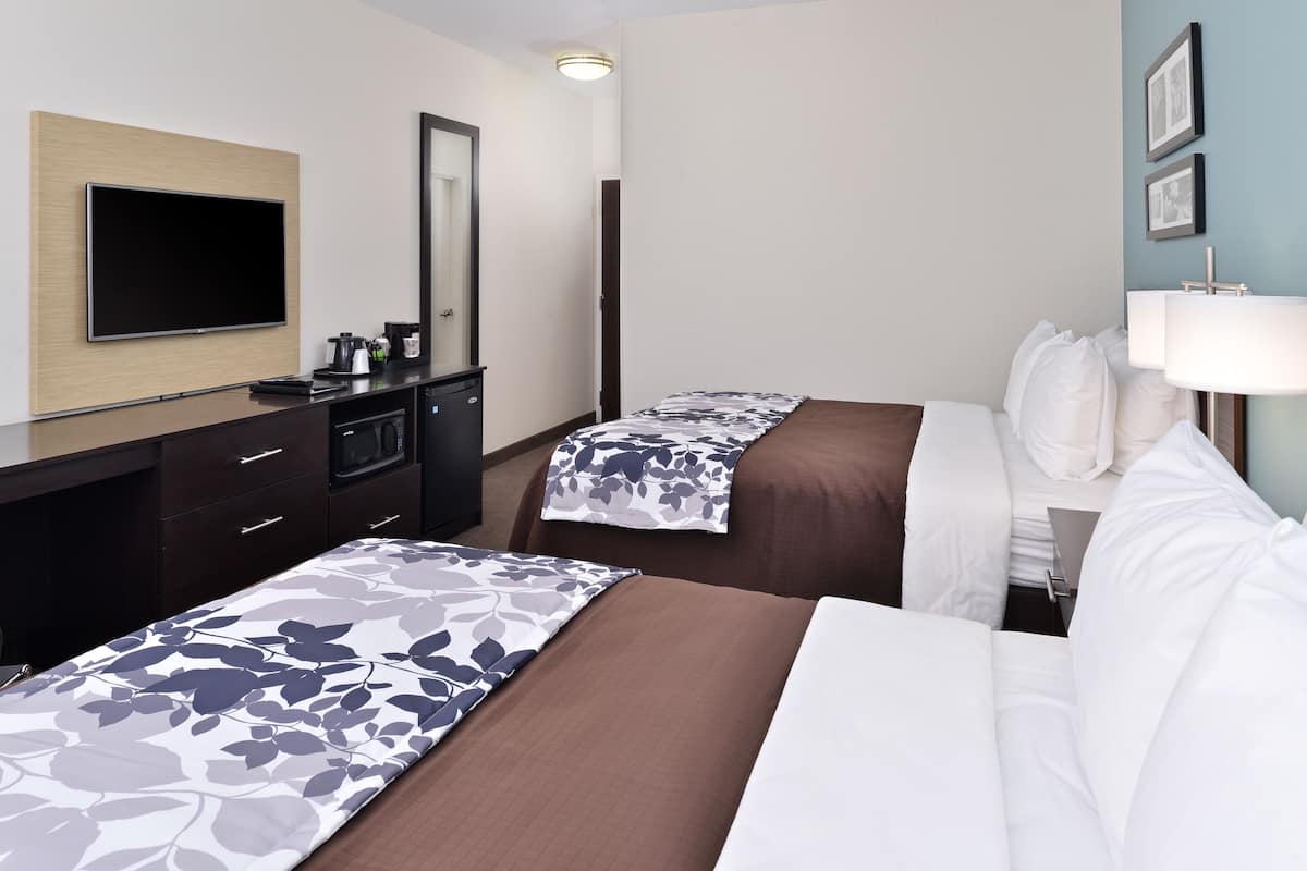 A hotel room with two beds, a flat-screen TV, a desk with a coffee maker, and a mirror.