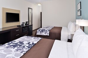 A hotel room with two beds, a flat-screen TV, a desk with a coffee maker, and a mirror.
