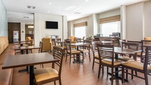 A hotel dining area with multiple tables and chairs, a flat-screen TV mounted on the wall, and a reception desk in the background. - Sleep Inn & Suites Meridian - Bonita Lakes (Meridian)