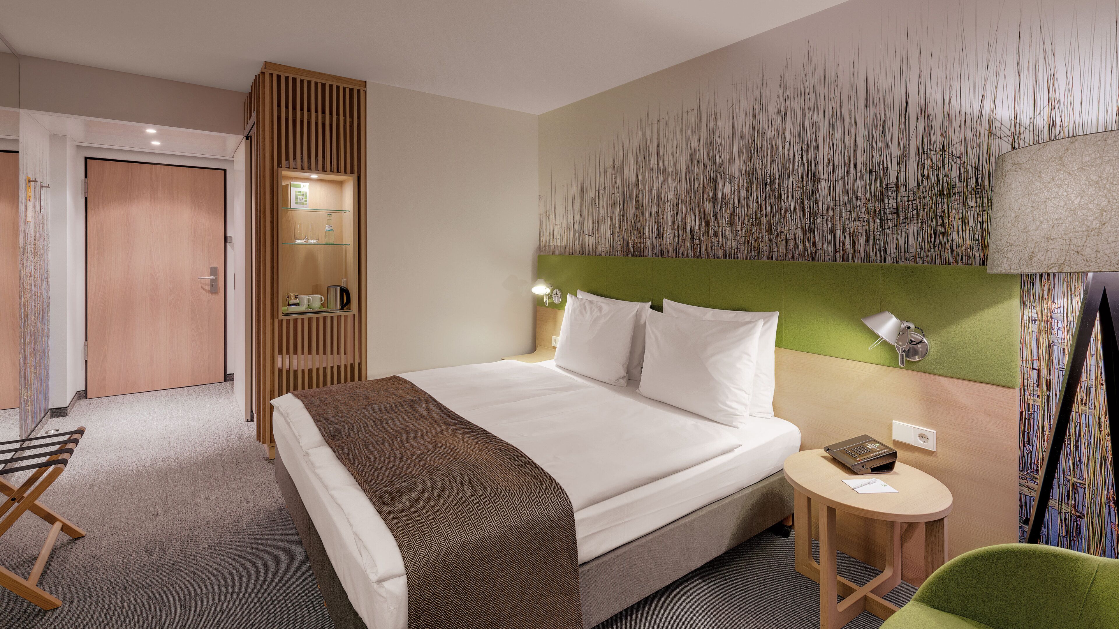 A hotel room with a bed, a bedside table, a chair, a wardrobe, and a wall with a textured design.
