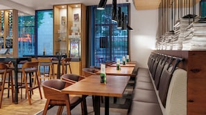 A modern restaurant interior with wooden tables and chairs, a bar area, and a view through large windows. - Holiday Inn Frankfurt - Alte Oper by IHG (Frankfurt)