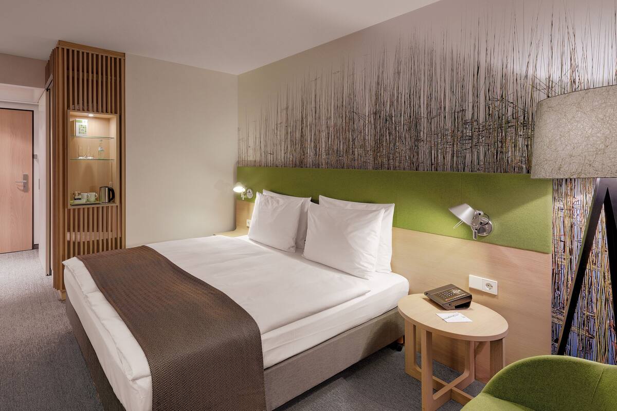 A hotel room with a bed, a small table, a chair, a wardrobe, and a wall with a textured design.